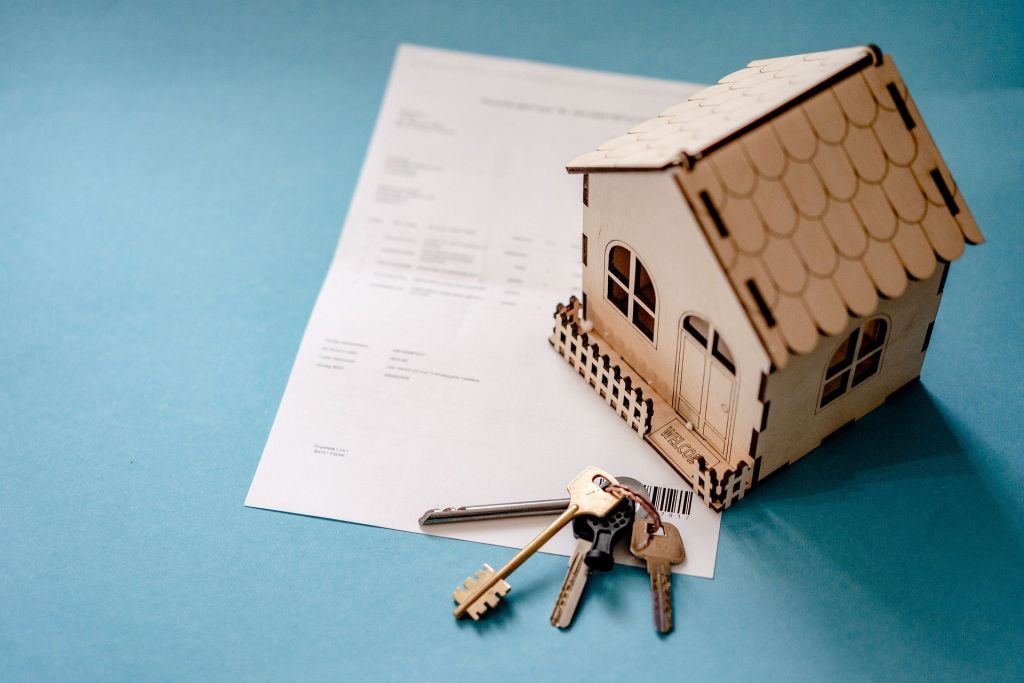 miniature wooden house with house keys and a contract next to it